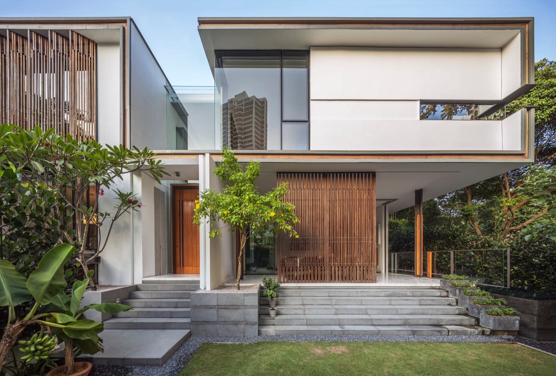 Two storey landed home with white volumes, timber screens and a landscaped entry